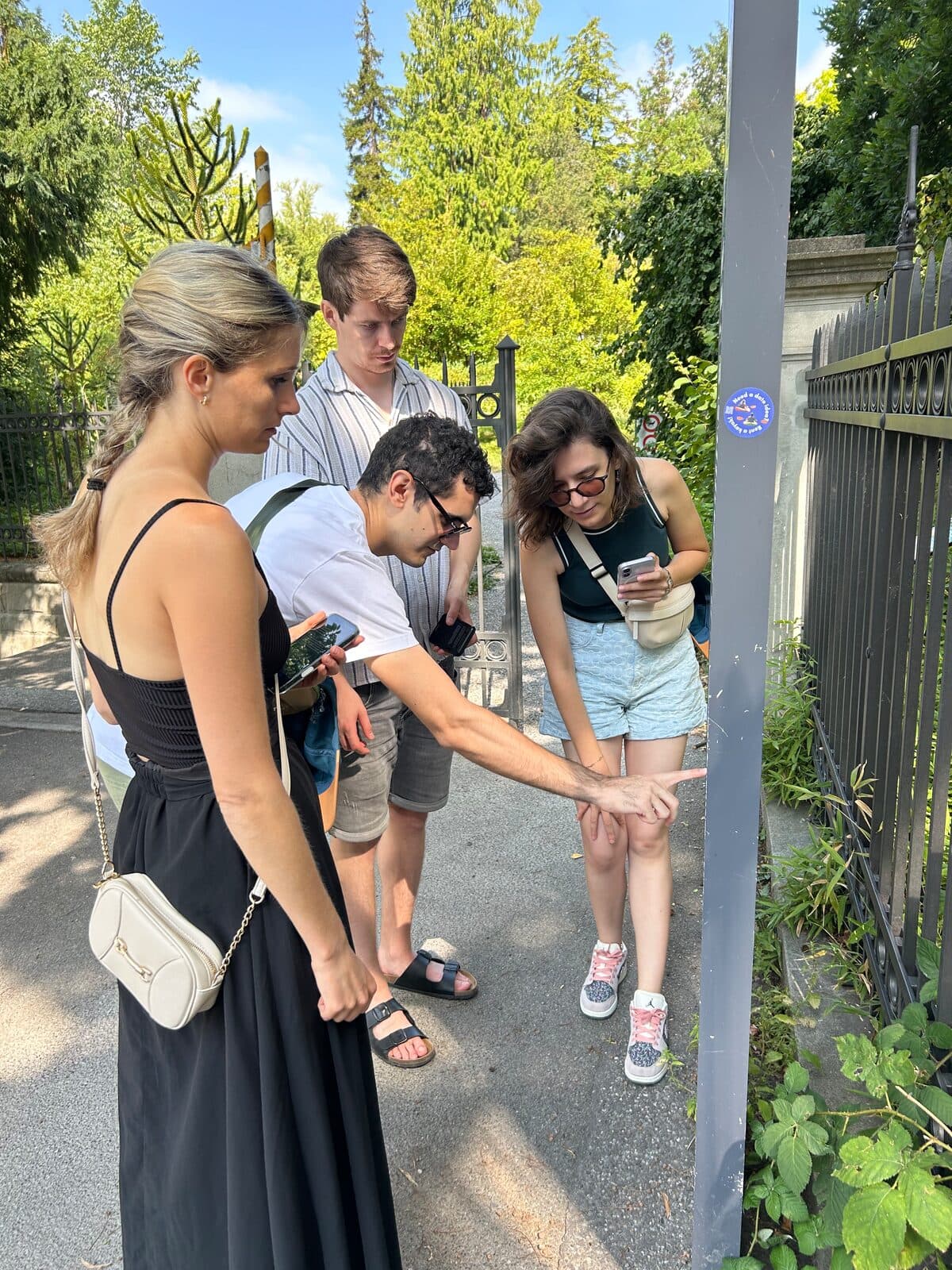 A team of four outside the Old Botanical Garden in Zürich, one of them pointing something out on a metal post.