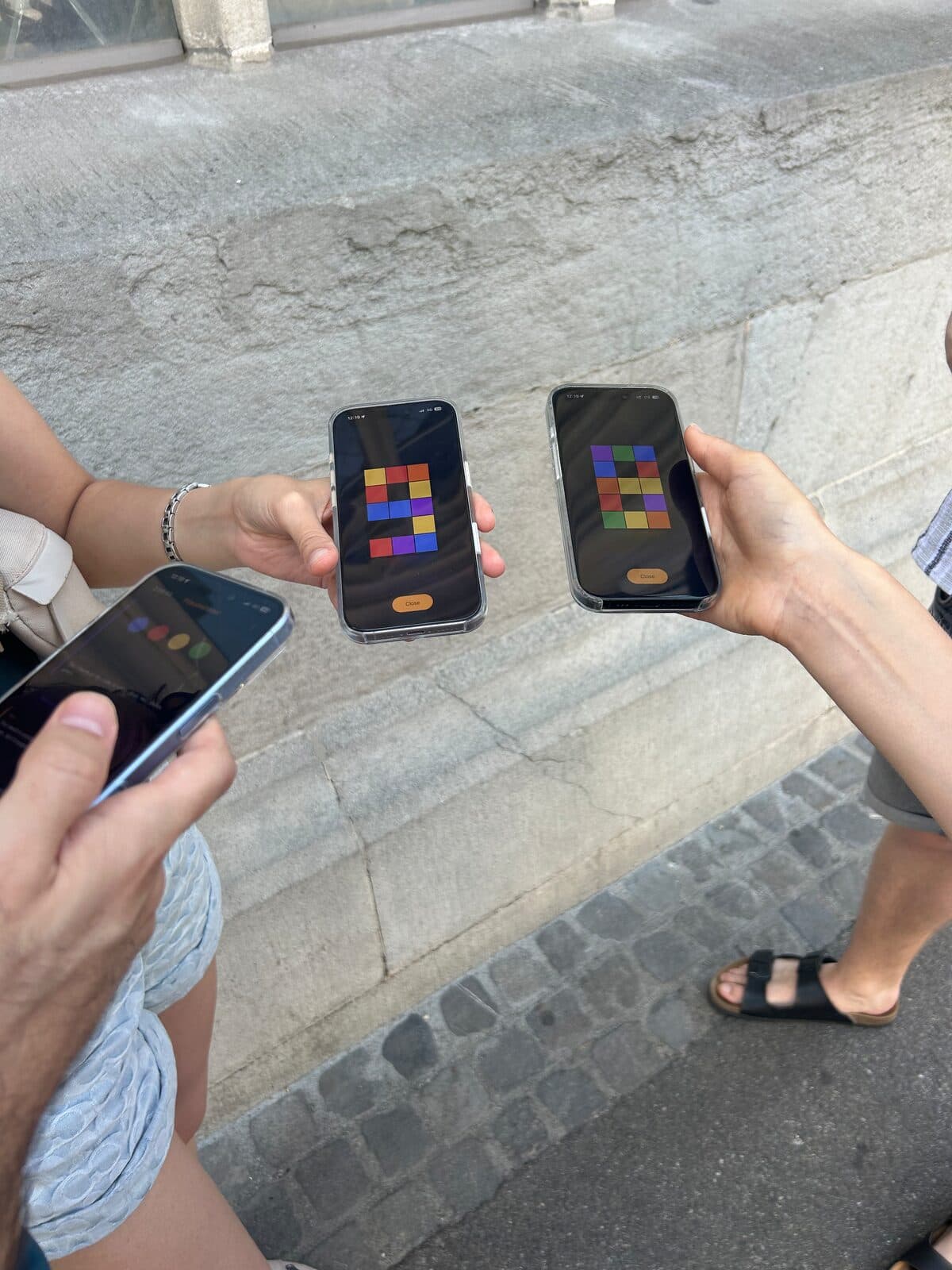 Players holding their phones side by side, each screen showing a different arrangement of coloured tiles.